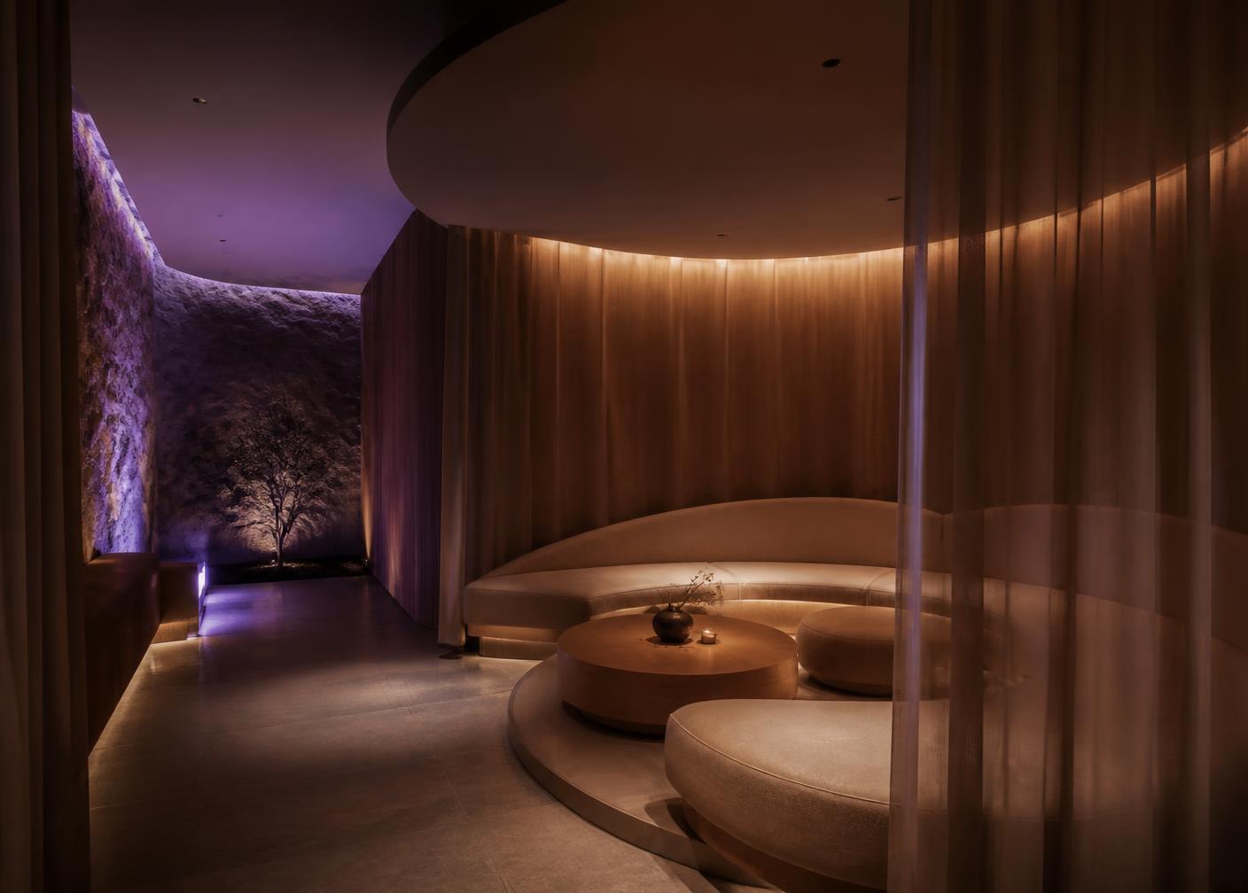 A luxury recovery lounge with curved seating, warm low light and acoustic drapery